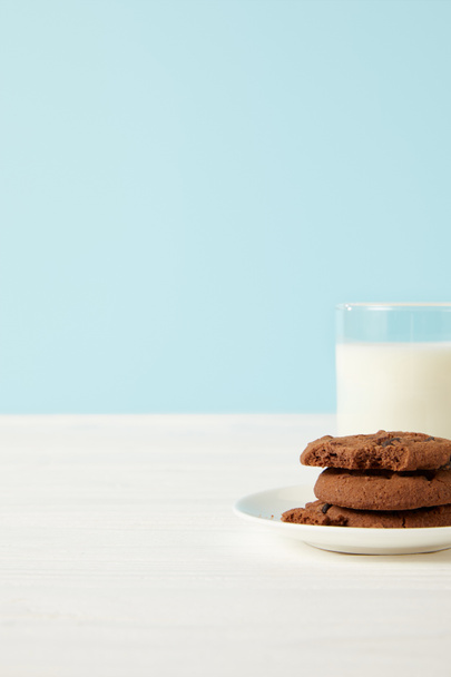 chocolate cookies on saucer and milk glass on blue background  - Fotó, kép