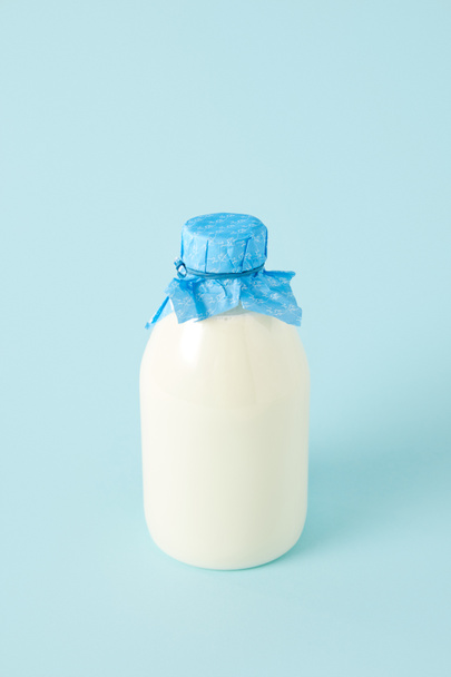 primer plano de leche fresca en botella envuelta por papel sobre fondo azul
 - Foto, imagen
