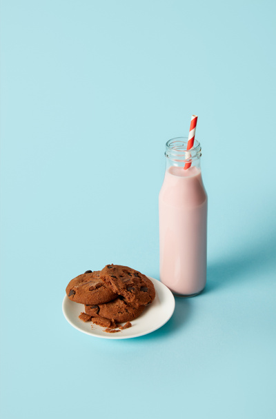 chocolate cookies in saucer and strawberry milkshake in bottle with drinking straw on blue background  - Fotó, kép