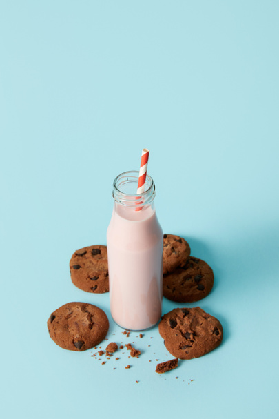 strawberry milkshake in bottle with drinking straw surrounded by chocolate cookies on blue background  - Foto, Imagem