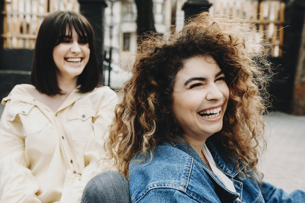Close up portrait of a curly cute woman laughing and looking away while in her back also laughing her brunette sister. - Fotografie, Obrázek