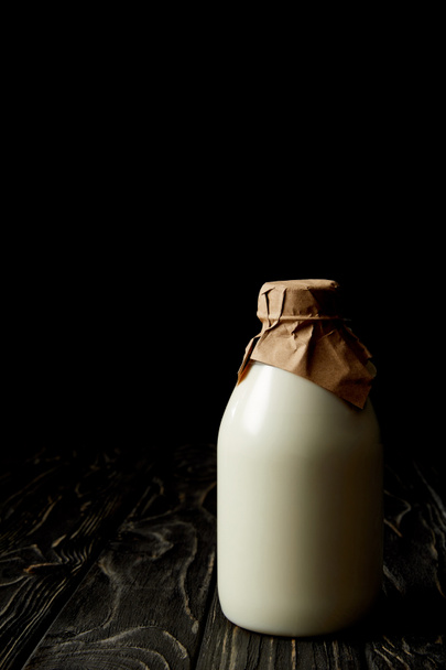 closeup view of fresh milk in bottle wrapped by paper on black background  - Photo, Image