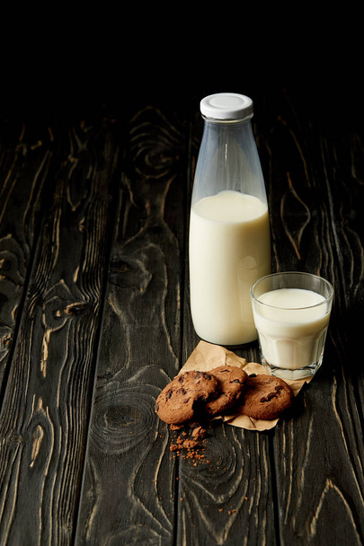 lähikuva suklaakekseistä, maidosta pullossa ja lasista puupohjalla
 - Valokuva, kuva