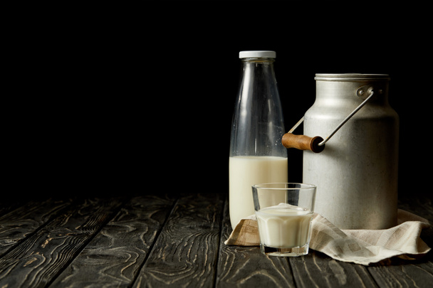 Milch in Flasche, Glas und Aluminiumdose auf Sacktuch auf schwarzem Hintergrund  - Foto, Bild