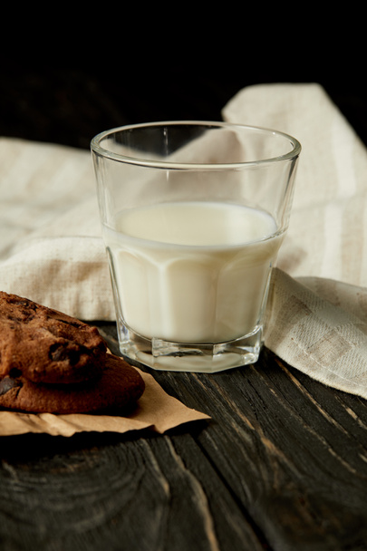closeup view of milk glass, chocolate cookies and sackcloth on black background  - Photo, Image