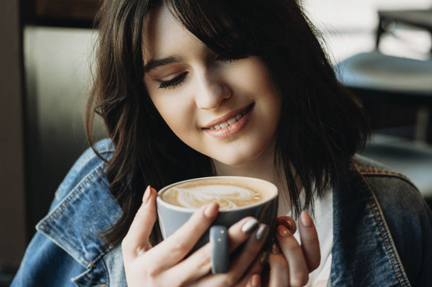 Красива молода дівчина з чорним коротким волоссям насолоджується чашкою кави, посміхаючись
 - Фото, зображення