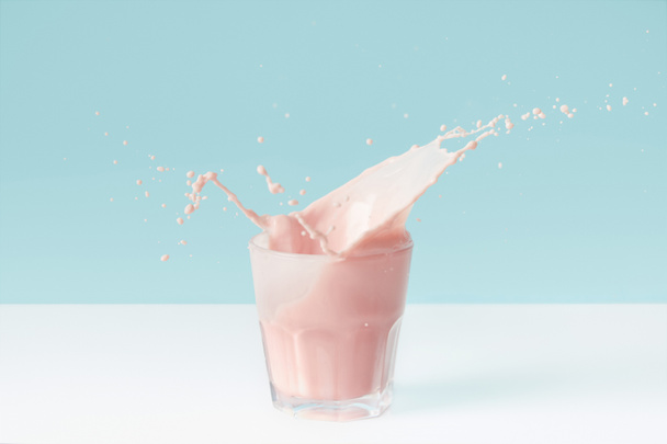 splashing drops of strawberry milkshake from glass on blue background  - Foto, Imagem