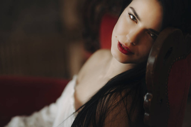 Bir sandalyede oturuyor ve kameraya bakarak kırmızı dudaklar kadın ile güzel bir portresi. - Fotoğraf, Görsel