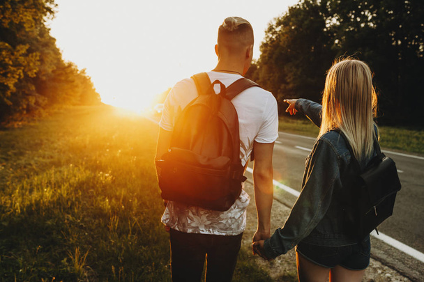 Back view of amazing caucasian couple where girl is showing the way to go on their adventure to his boyfriend in the way of a beautiful sunset. - Фото, зображення