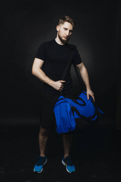 Спортивный молодой человек, серьезно смотрящий в камеру и держащий на плече спортивную сумку
. - Фото, изображение