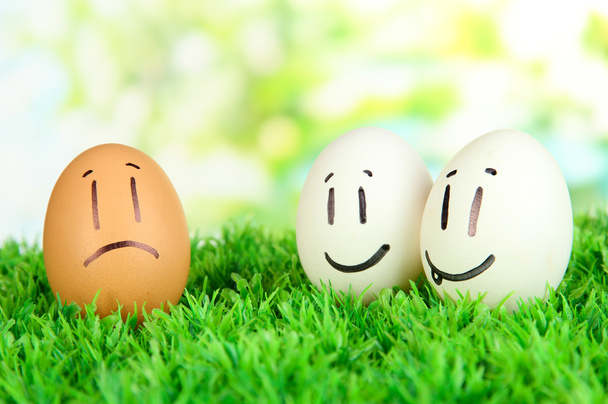 Eggs with funny faces on grass on bright background - Foto, Imagem