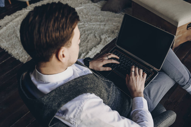 ΠΙΣΩ ΟΨΗ πορτρέτο ενός άνδρα ντυμένος με το κουστούμι που εργάζεται στο φορητό υπολογιστή, ενώ κάθεται σε έναν καναπέ. - Φωτογραφία, εικόνα