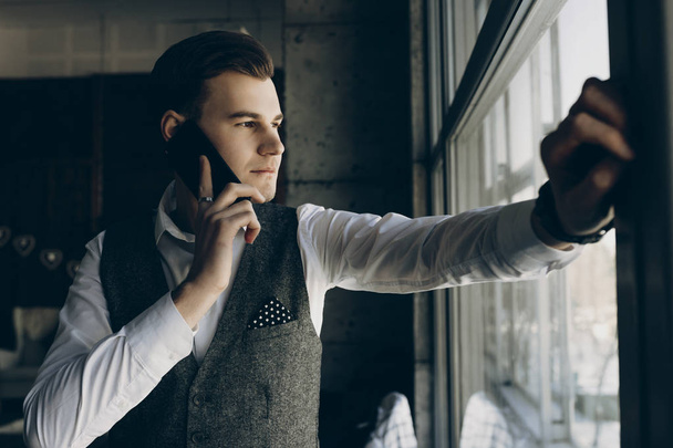 Νεαρός επιχειρηματίας, μιλώντας στο τηλέφωνο και να αναζητούν μέσα από το παράθυρο. - Φωτογραφία, εικόνα