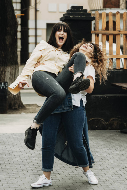 Full length portrait, of a curly girl holding in her arms another short haired girl ,laughing. - Foto, Imagem