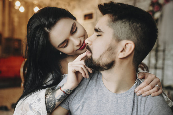 Close up portrait of a amazing couple sitting in a chair where woman is embracing from back her love and playing with his lips smiling. - Zdjęcie, obraz