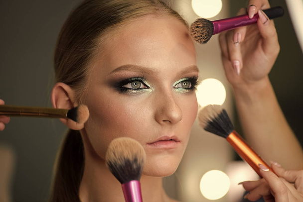 Beautiful young woman with makeup brushes around face. - Foto, Imagen