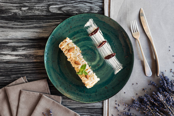süßes, schmackhaftes Dessert mit Mandeln und Minze auf Teller und Gabel mit Messer auf Holztisch  - Foto, Bild