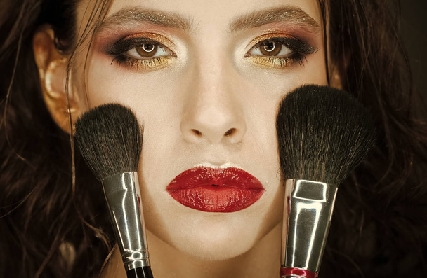 Girl with makeup brushes apply powder on face , cosmetics. Girl with art makeup and red lips. - Photo, Image