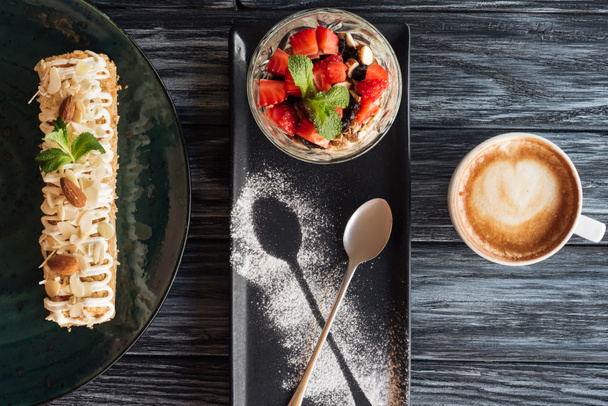 bovenaanzicht van zoete gourmet desserts en kopje koffie op houten tafel  - Foto, afbeelding