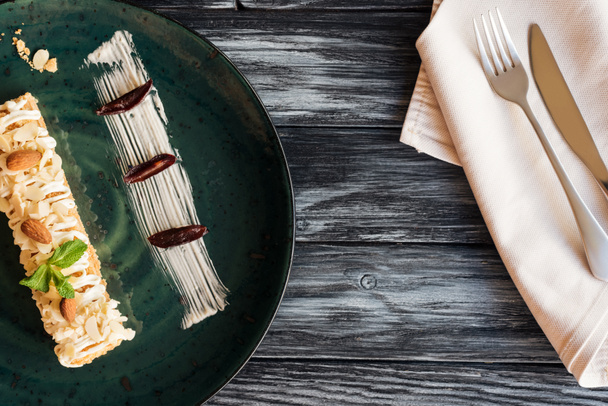 вид зверху на гастрономічний солодкий десерт з мигдалем і м'ятою на тарілці і виделкою з ножем на дерев'яному столі
 - Фото, зображення