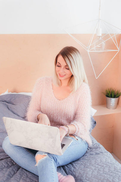 Happy casual beautiful woman working on a laptop sitting on the bed in the hous - Foto, Bild