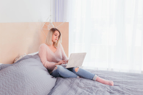 Happy casual beautiful woman working on a laptop sitting on the bed in the hous - 写真・画像