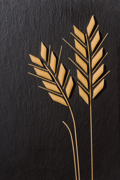 pohled shora z uší pšenice vyrobené z nevařené těstoviny na černém povrchu - Fotografie, Obrázek