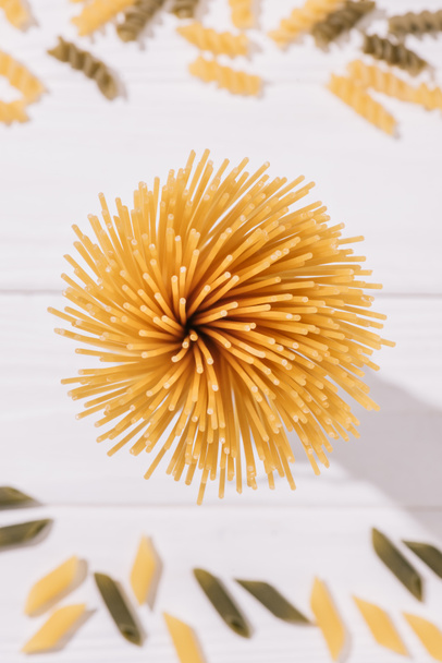 top view of bunch of raw spaghetti on white wooden tabletop with other types of pasta - Фото, изображение