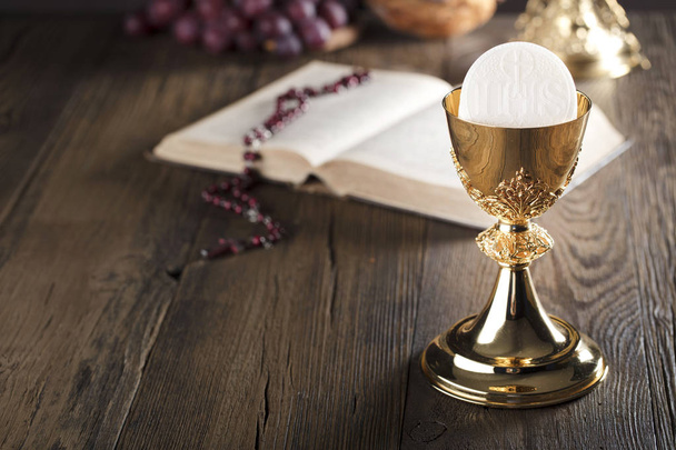 First holy communion theme. Holy Bible, rosary and golden chalice. Bread and grapes  symbols of Christianity. - Photo, Image