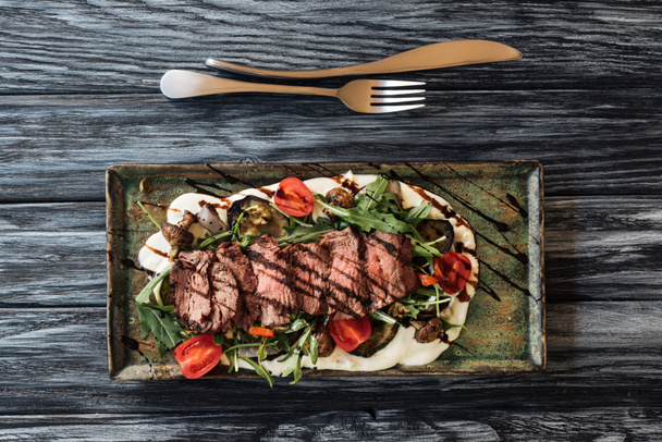vista dall'alto di bistecca, verdure e forchetta di New York tagliata a fette gourmet con coltello sul tavolo di legno
  - Foto, immagini