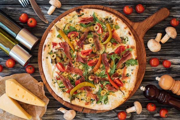 vista superior de la deliciosa pizza horneada con verduras, queso y carne en la tabla de cortar de madera
   - Foto, Imagen