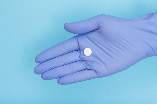 Close up hand of female doctor in blue latex glove with white pill on the palm of her hand. Legal drug store concept - Foto, Bild