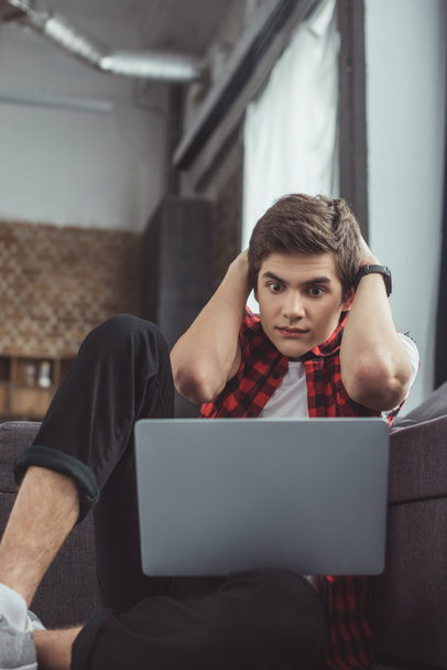 shocked teenager looking at laptop while sitting on floor - Фото, зображення