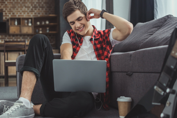 handsome smiling teenager listening music with earphones and using laptop   - Φωτογραφία, εικόνα