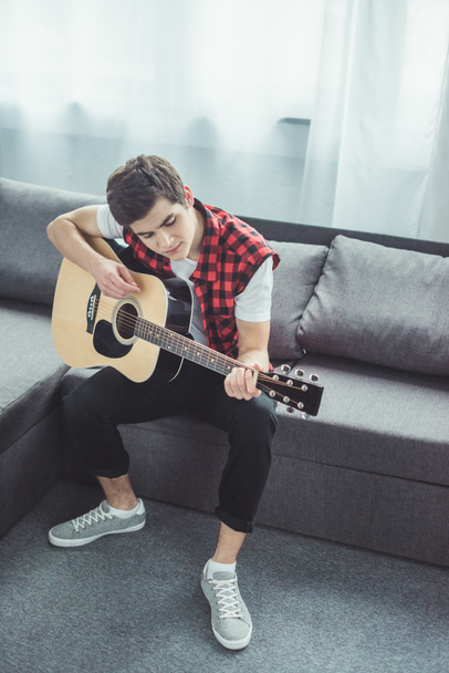 male teenager playing acoustic guitar on sofa at home - Zdjęcie, obraz