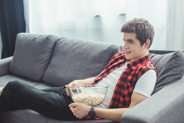 teenager with popcorn watching tv and sitting on sofa at home - Fotó, kép