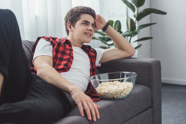 smiling male teenager with popcorn watching movie at home - Valokuva, kuva