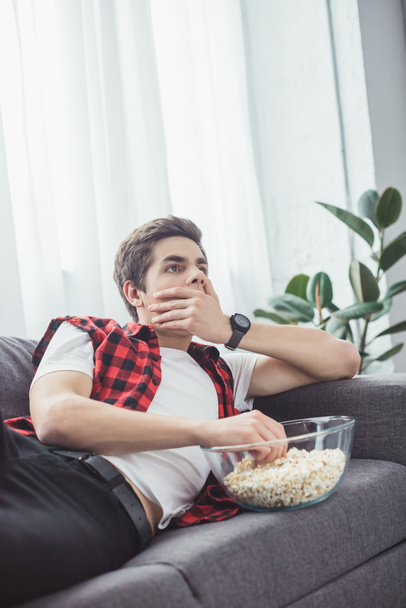 shocked teen boy with popcorn watching movie on sofa at home - Фото, зображення