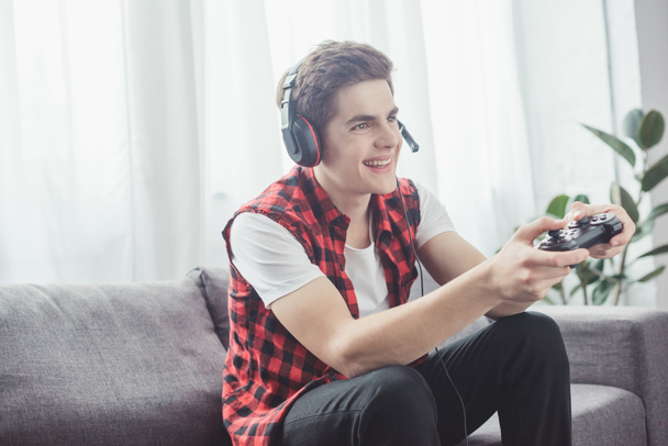 happy teenager with headset playing video game with joystick at home - Photo, image