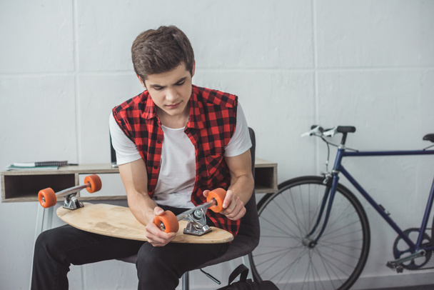 young skateboarder repairing his longboard at home - Photo, Image