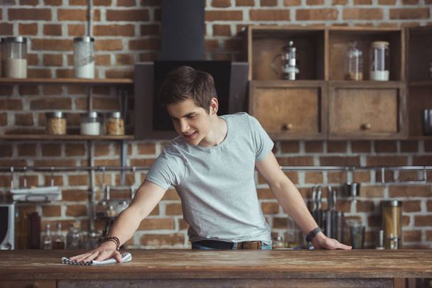 handsome teenager cleaning table with rag in kitchen - Photo, Image