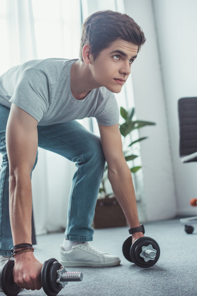 handsome teenager squatting with dumbbells at home - Photo, Image