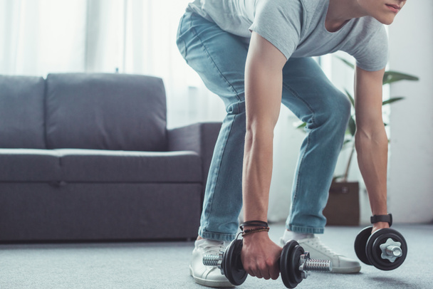 cropped view of teen boy squatting with dumbbells at home  - Foto, Imagem