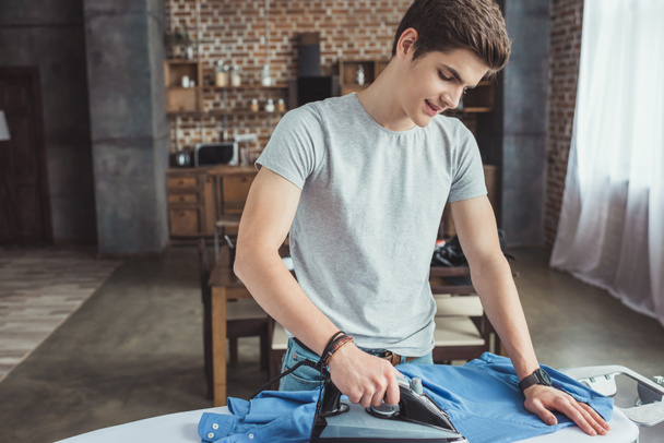 handsome teenager ironing blue shirt with iron - Foto, afbeelding