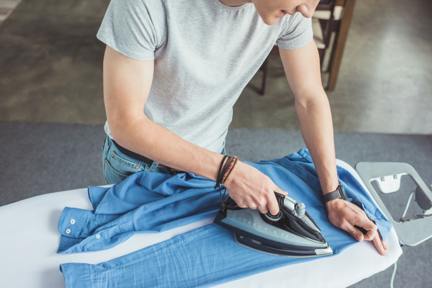 cropped view of teenager ironing blue shirt with iron at home - 写真・画像