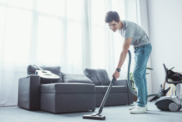 teenager vacuuming floor in living room with vacuum cleaner - Fotó, kép
