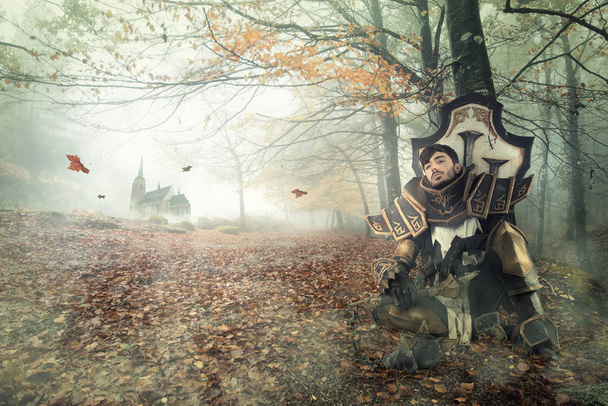 Young man cosplaying with fantasy knight costume resting in a dark forest - Photo, Image