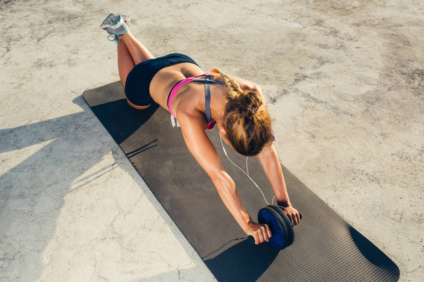 high angle view of sportswoman in earphones doing exercise with abs roller on fitness mat  - Foto, Bild