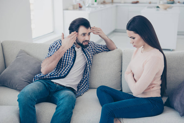 Portrait of  bearded discontent man gesturing with hands pointing on brain saying speaking arguments to his upset girlfriend sitting with crossed folded hands, couple having scandal - Foto, Imagem
