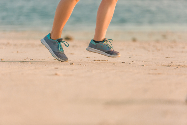 cropped shot of female jogger in sneakers running on sandy beach with sea behind  - Fotoğraf, Görsel